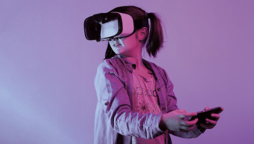 Mädchen mit aufgesetzter VR-Brille und einem Smartphone in der Hand steht vor einem lila Hintergrund.