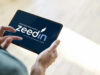 Hände halten ein Tablet mit dem zeedin-Logo in der Hand.