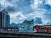 Eine Bahn fährt über eine Brücke in Hamburg, mit der gläsernen Fassade der Elbphilharmonie und modernen Hochhäusern im Hintergrund.