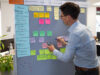 Mitarbeiter steht vor einer Pinnwand mit Post Its für einen Design Sprint.