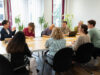 9 Personen sitzen um einen Konferenztisch und diskutieren.